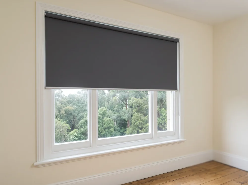 Flat blockout roller blind lowered over a sash window in a Newlands bedroom, oak canopy visible outside